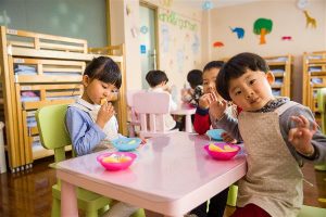 Three young children at a preschool share a healthy snack.