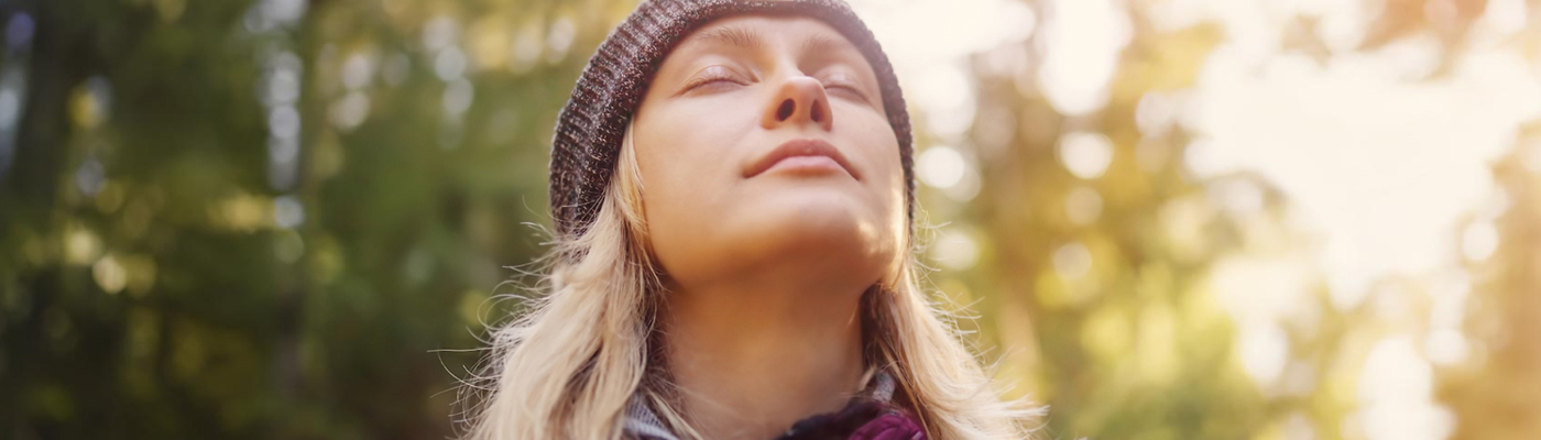close up of young woman, wearing flannel shirt, knit hat, head tilted back, eyes closed, peaceful and relaxed expression, meditating outdoors in nature