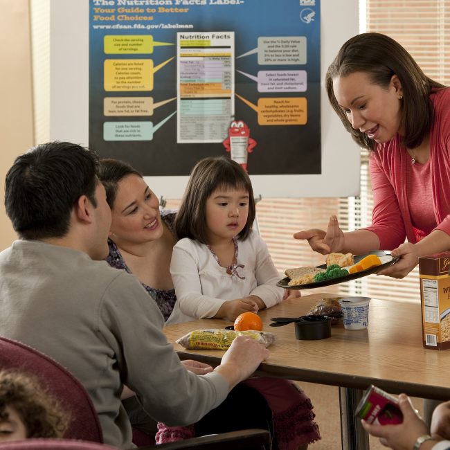 Educator sharing food nutrition information with a young family in school setting