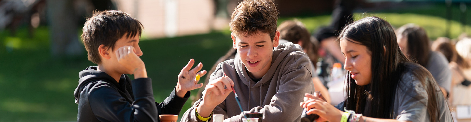 Main heading image showing young teens talking and working on a project together, with many other kids in the background