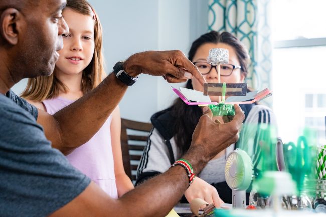 an adult working on a craft project with two young kids