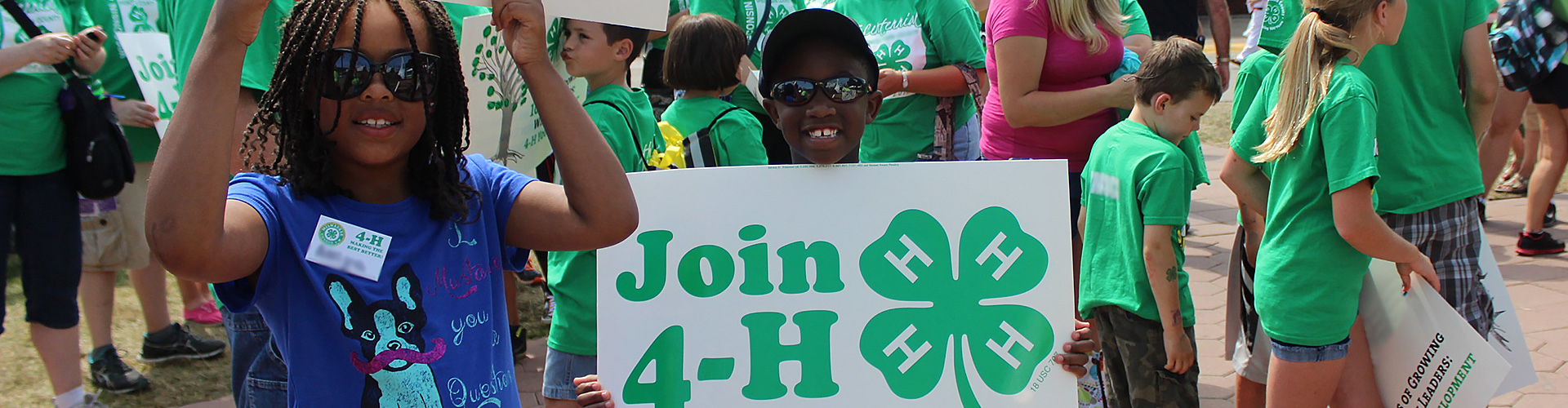 main header image showing many adults and young people, likely waking in a parage, holding signs to 'Join 4-H' and has a variety of kids ages and ethnicities in the group.